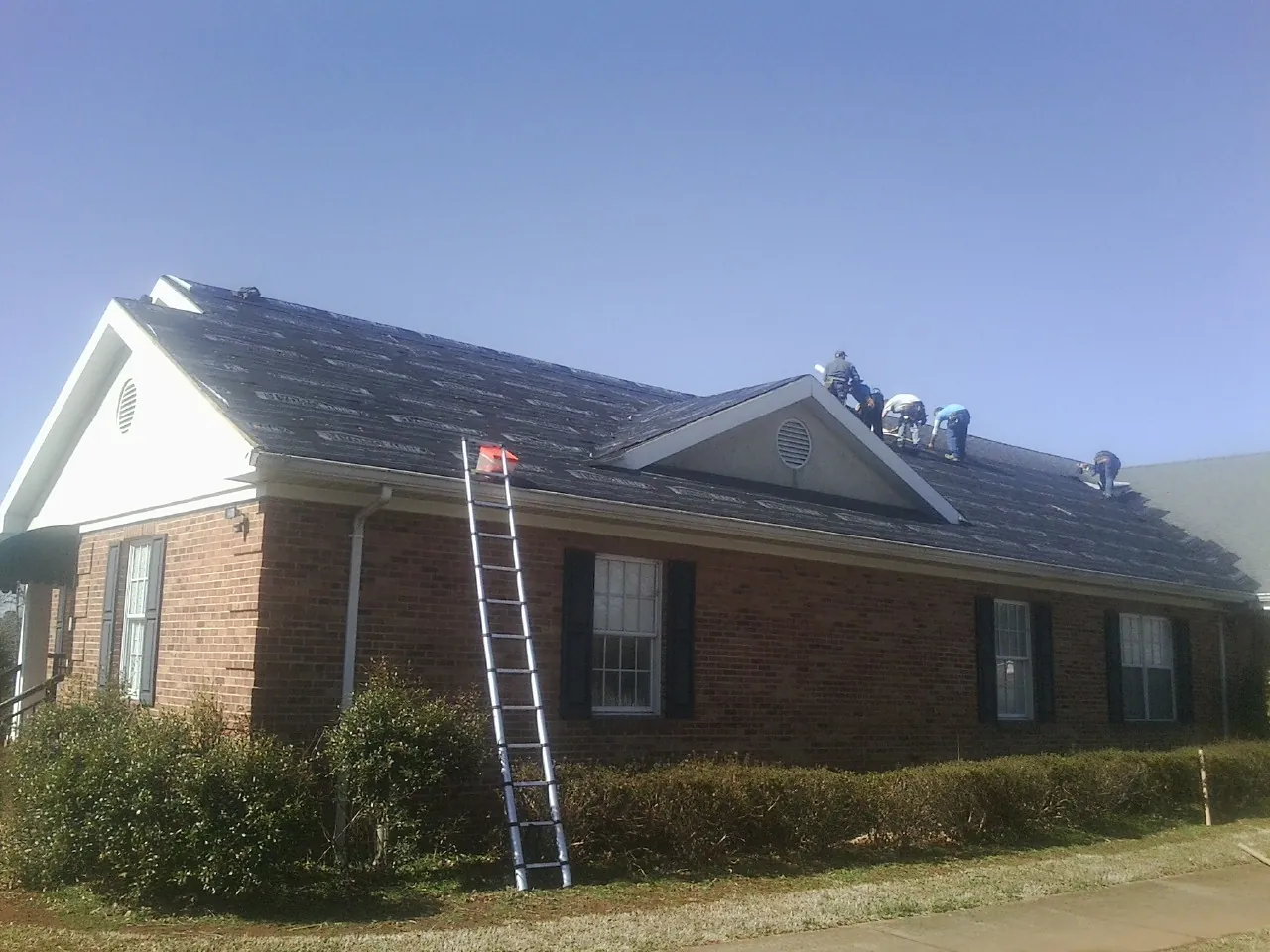 Crew tearing shingles off a brick ranch roof with a ladder set — Metal Roof Repair work by our crew in Ringwood