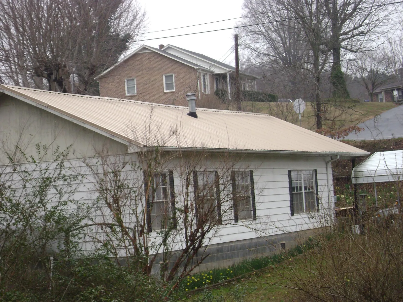 Tan metal roof on a white sided house set into a hillside — Commercial Roofing by Roofing Brothers in Ringwood